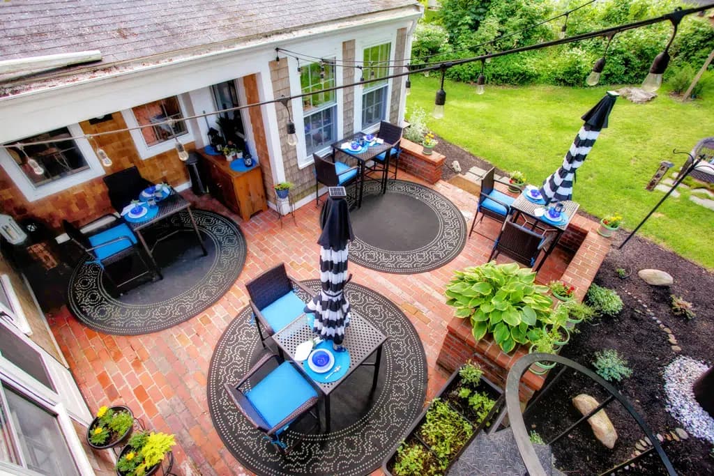 Aerial View of Brick patio, square black tables, round black and white rugs with patio chairs and lime green cushions with a backdrop of the cedar shake building.