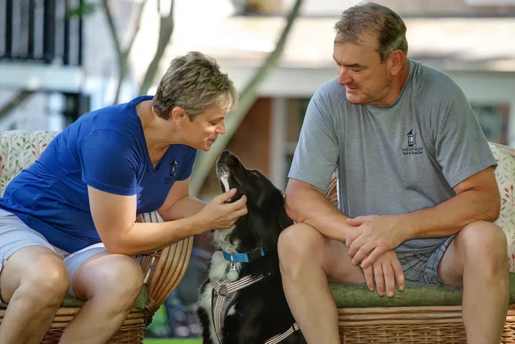 Innkeepers sitting in yard on wicker chairs with hugging black dog