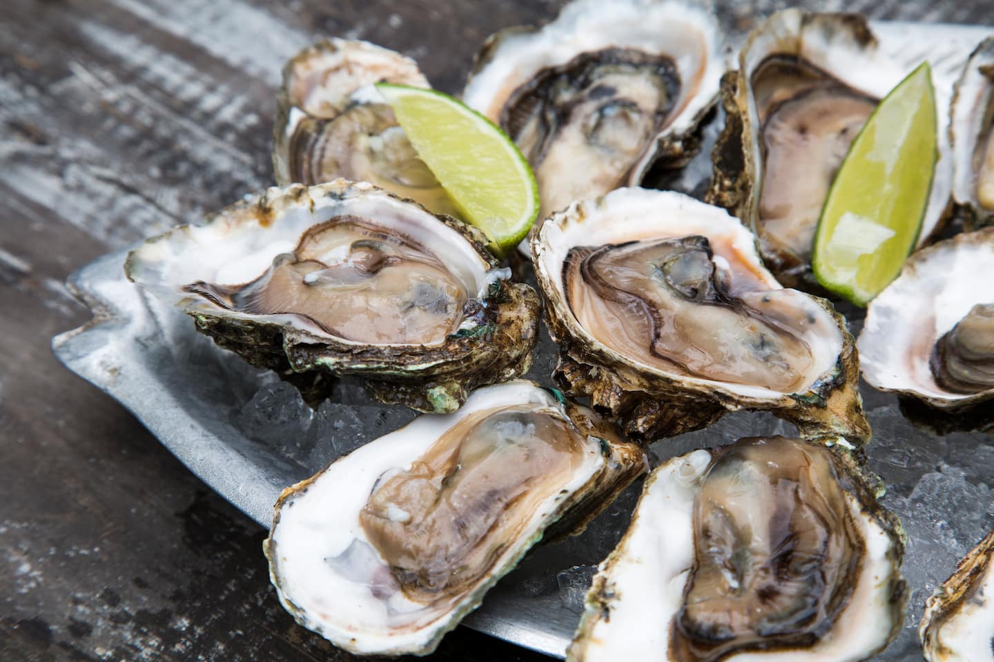 A plate of fresh oysters garnished with lime wedges on ice.