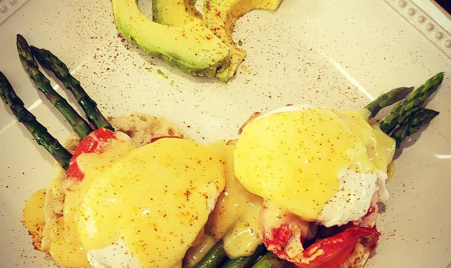 Lobster Benedict on white plates with sauce and asparagus