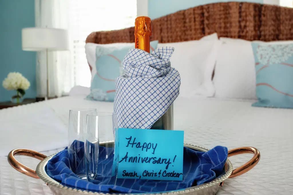 Happy anniversary note, with bottle of champagne sitting on tray on bed with white linens