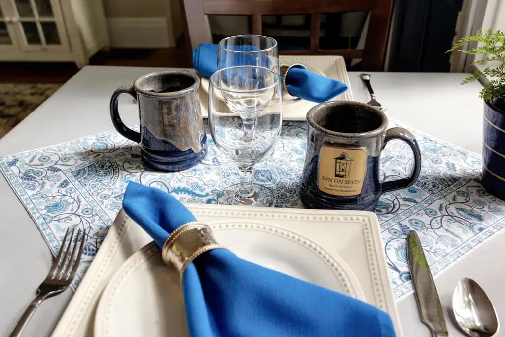 Breakfast Table for two set with white table cloth and blue linens and custom Inn Mug