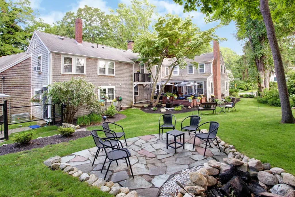 View of back courtyard of inn, brick patio, green grass, with metal tables and chairs