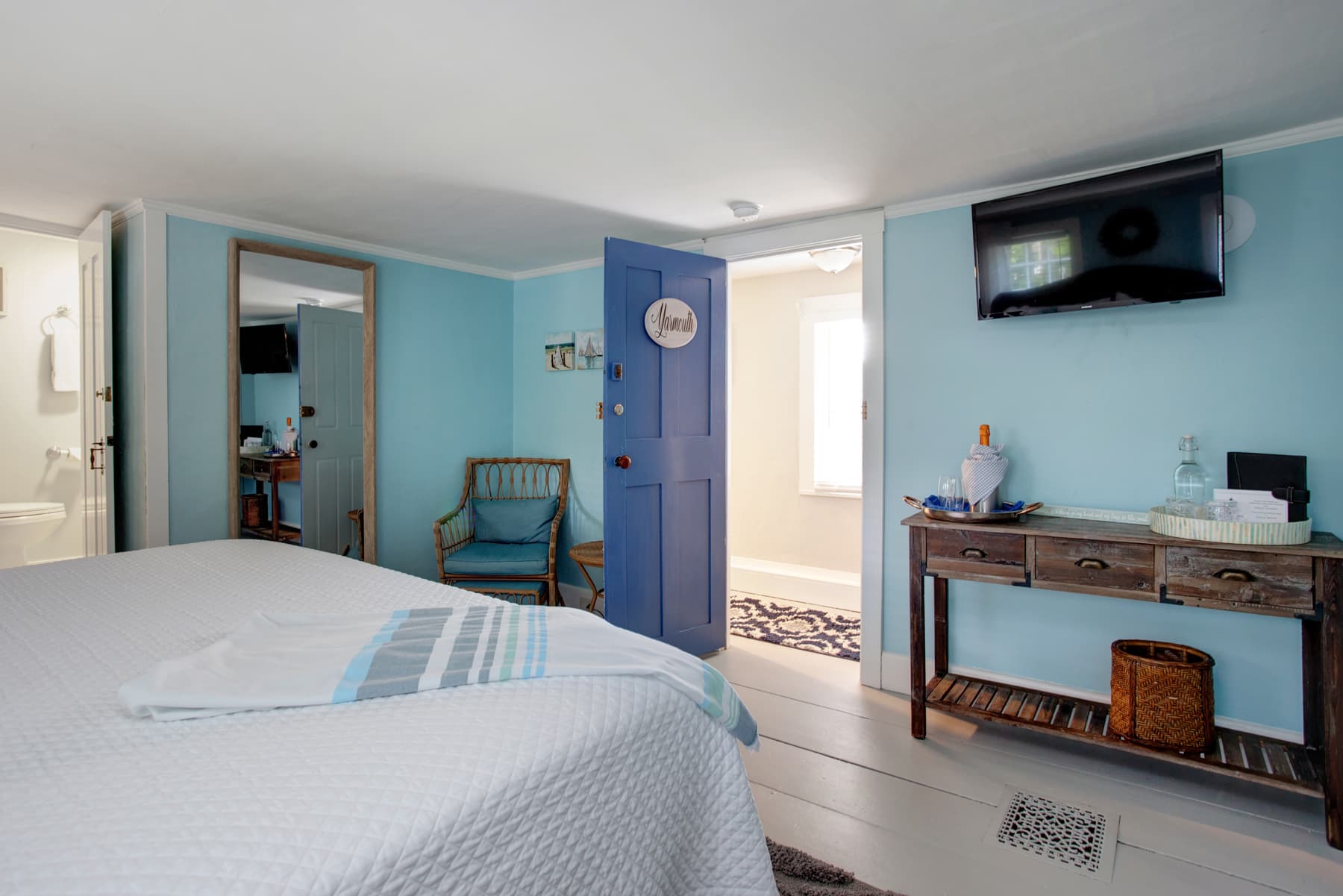 View of wall opposite bed with console table, wall-mounted flat-screen TV, and doorway leading to hall