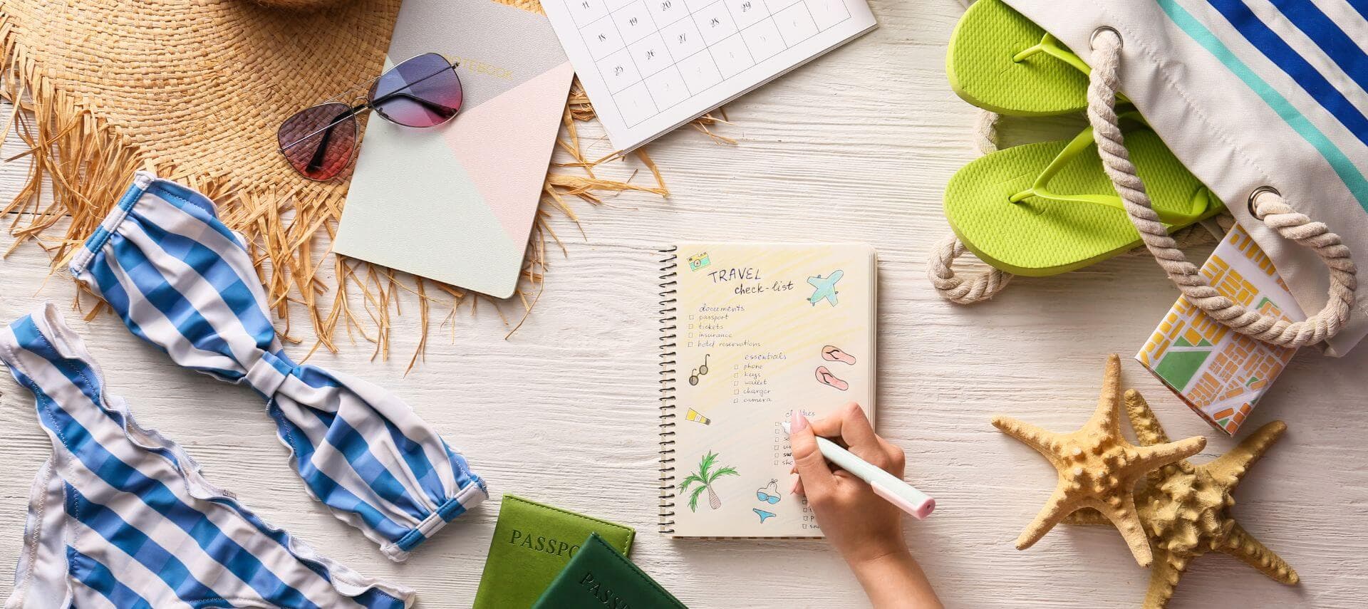 A flat lay of a beach-themed planning setup featuring a notebook, sunglasses, a calendar, flip-flops, a bikini, and a starfish.