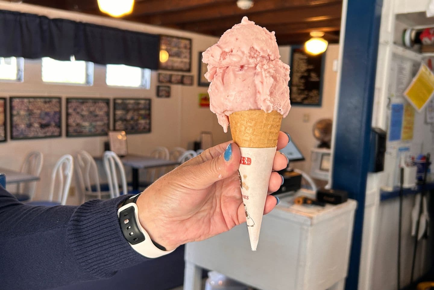 A hand holding an ice cream cone with pink ice cream in a cafe. A hand holding an ice cream cone with pink ice cream in a cafe.