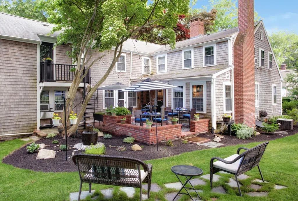View of back courtyard of inn, brick patio, green grass, with metal tables and chairs