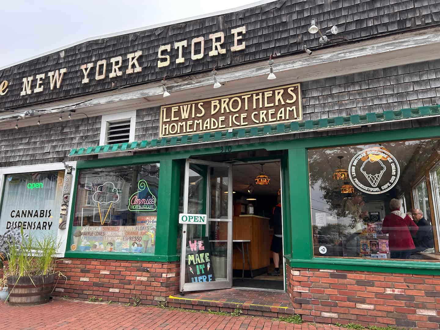 A charming ice cream shop, Lewis Brothers, with a green entryway and a welcoming "Open" sign, located in a rustic building.